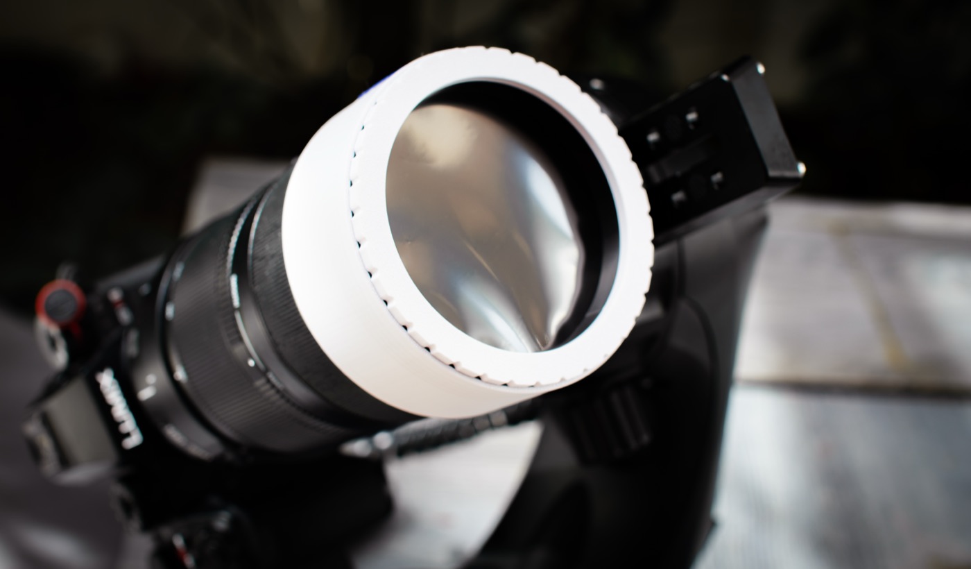 A white 3D-printed solar filter pushed onto a telephoto lens on a tripod.