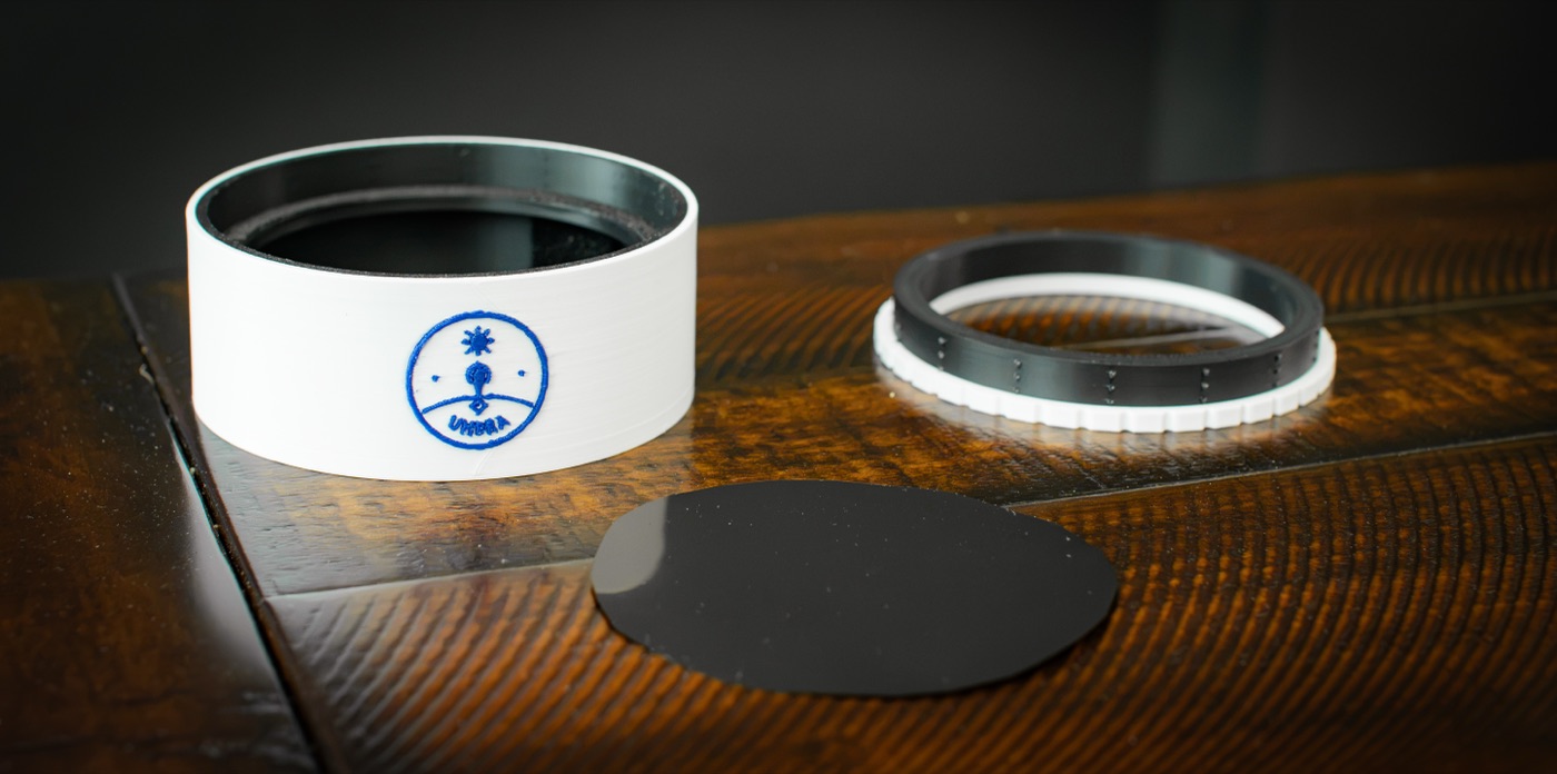 The three pieces laid out on a bench: the printed body with the Umbra badge, the printed clamping ring, and a cut disc of solar film.